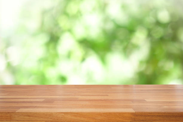 istock Empty wooden table and blurred green leaves bokeh  background 998264396