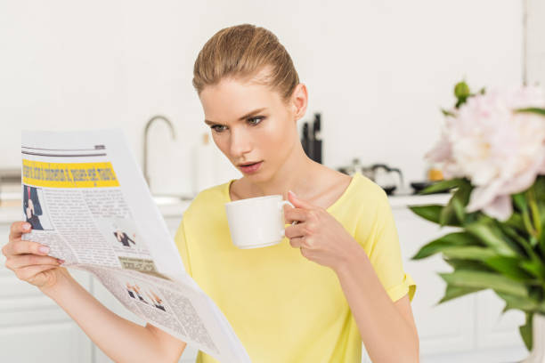 istock young woman reading newspaper and drinking coffee at table with flowers at kitchen 998267620