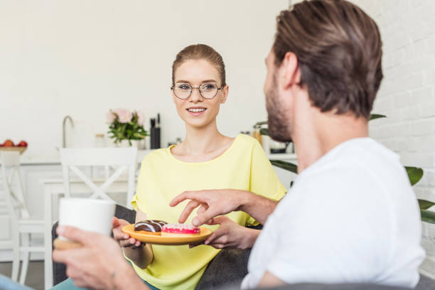 istock man with coffee cup taking donut from plate while his girlfriend holding it 998268068