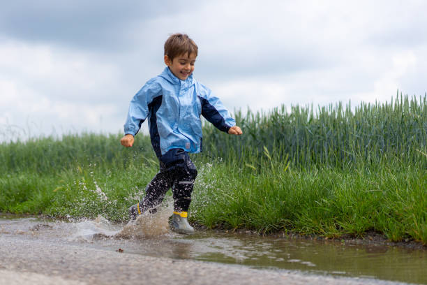 istock smiling little boy running through rain puddle splashing 998271858