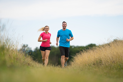 front shot of couple running in grassland rural outdoor setting overcast sky workout together man and woman jogging shallow focus