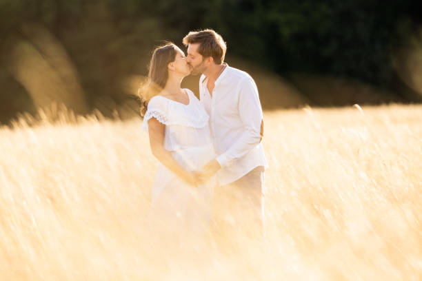 istock pregnancy, couple kssing in bright summer sunlight in high grass 998274702