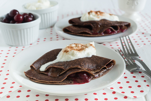 two portions of chocolate crepes with chocolate sauce, cherries and whipped cream on a plates