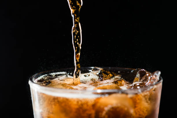istock stream of cola is poured into a glass with ice 998279632