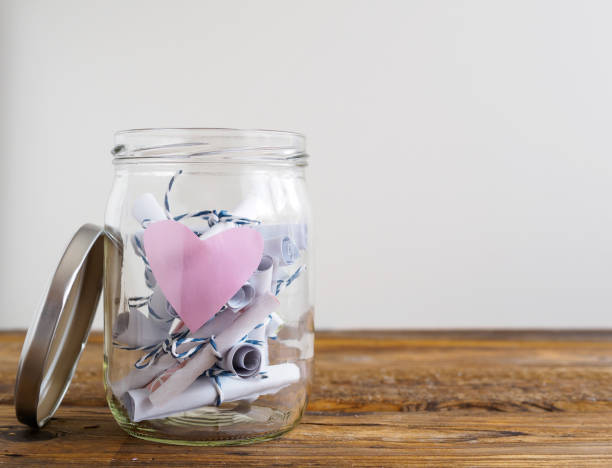 Jar with pink heart and rolled-up notepads Mason jar, notepad, twine, bow, table, white background, love, heart embassy photos stock pictures, royalty-free photos & images