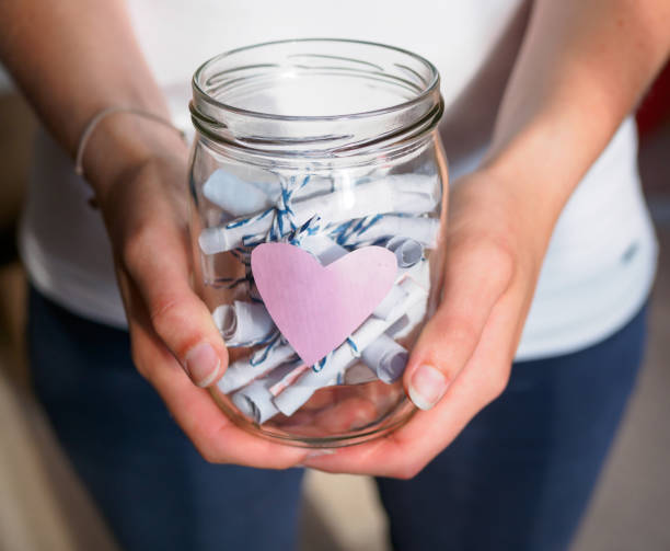 woman holds a jar with pink heart and curled notes in her hands - paper glass imagens e fotografias de stock