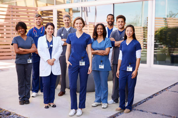 Healthcare team with ID badges stand outdoors, full length Healthcare team with ID badges stand outdoors, full length hands in pockets stock pictures, royalty-free photos & images