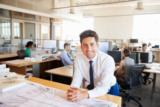 istock Young male architect in busy office smiling to camera 998324718