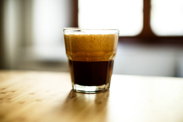 A glass of iced espresso lying on a wooden table A glass of iced espresso lying on a wooden table in front of a window freddo cappuccino stock pictures, royalty-free photos & images