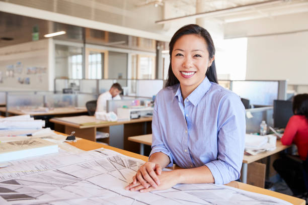 Female Asian architect smiling to camera in open plan office Female Asian architect smiling to camera in open plan office chinese woman stock pictures, royalty-free photos & images