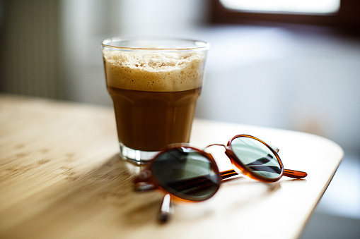 A glass of iced espresso and a pair of sunglasses lying on a wooden table