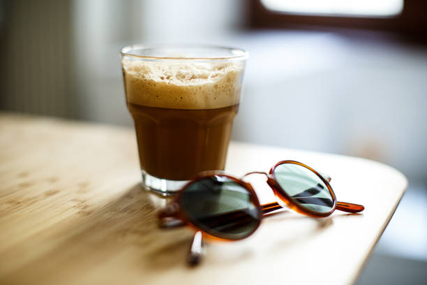 A glass of iced espresso and a pair of sunglasses lying on a wooden table A glass of iced espresso and a pair of sunglasses lying on a wooden table freddo cappuccino stock pictures, royalty-free photos & images