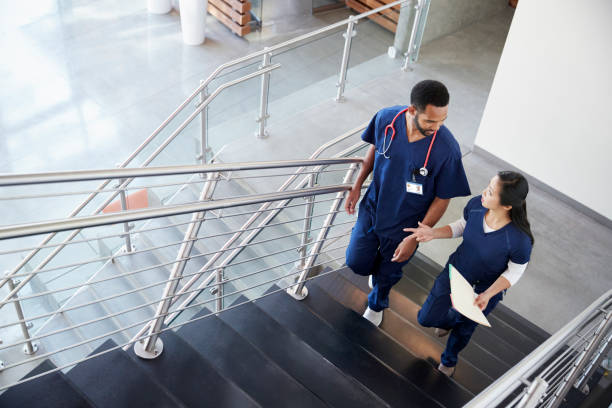 two healthcare colleagues talking on the stairs at hospital - doctor asian ethnicity chinese ethnicity young adult imagens e fotografias de stock