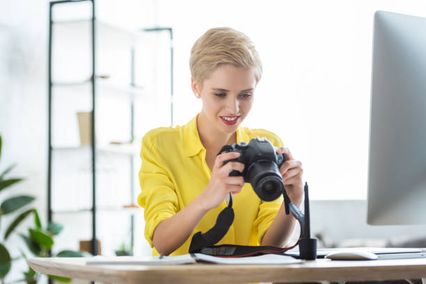 istock smiling female photographer looking at camera screen at table with computer 998344416