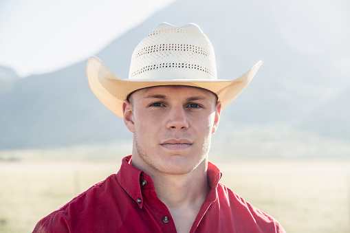 A man in a cowboy hat takes a selfie in front of a mountain.