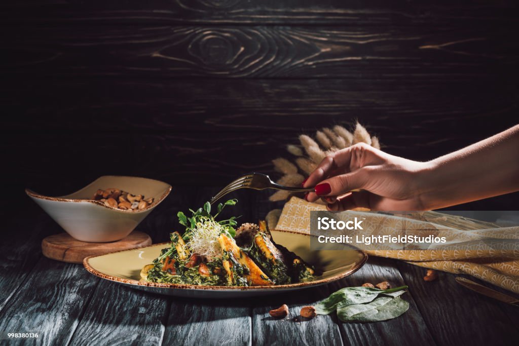 cropped image of woman eating panikesh with cashew nuts and spinach by fork over table Adult Stock Photo
