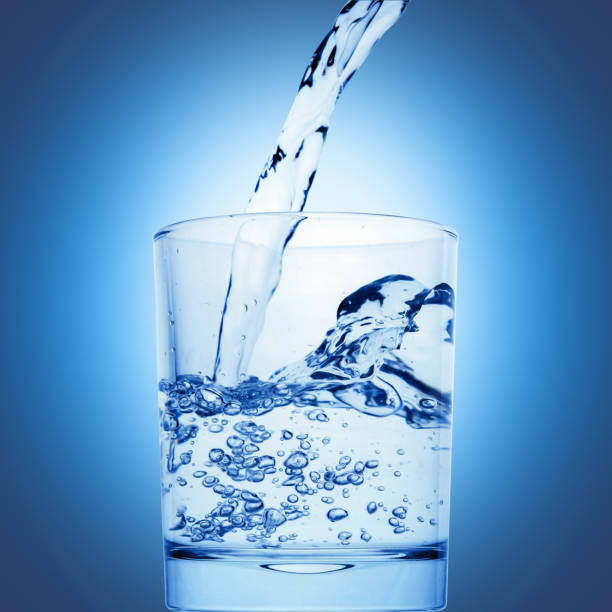 istock Water splash flowing into glass isolated on shining deep blue background 998389630