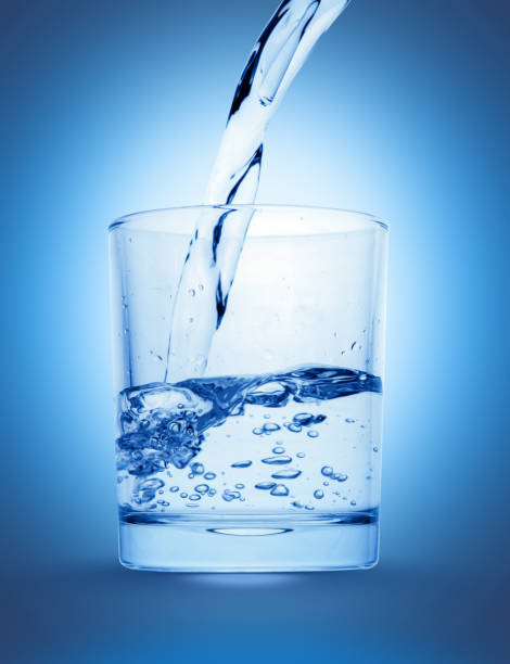 istock Water splash flowing into glass isolated on shining deep blue background 998389652