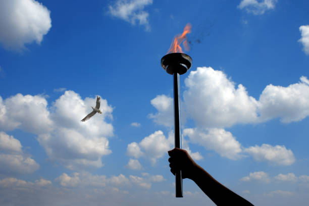 istock Close up hand holding burning flaming torch over cloudy sky 998410670