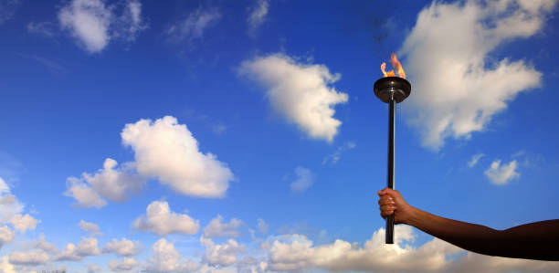 istock Close up hand holding burning flaming torch over cloudy sky 998410890