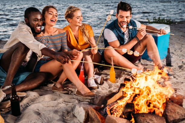 istock happy young multiethnic friends roasting marshmallows at bonfire on beach at sunset 998419172