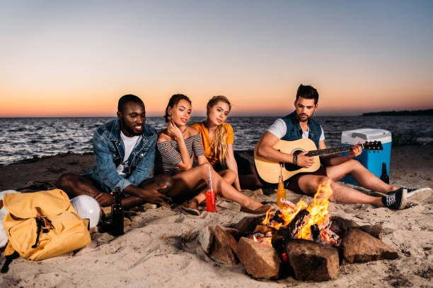 istock young multiethnic friends enjoying guitar and spending time together on sandy beach at sunset 998419306