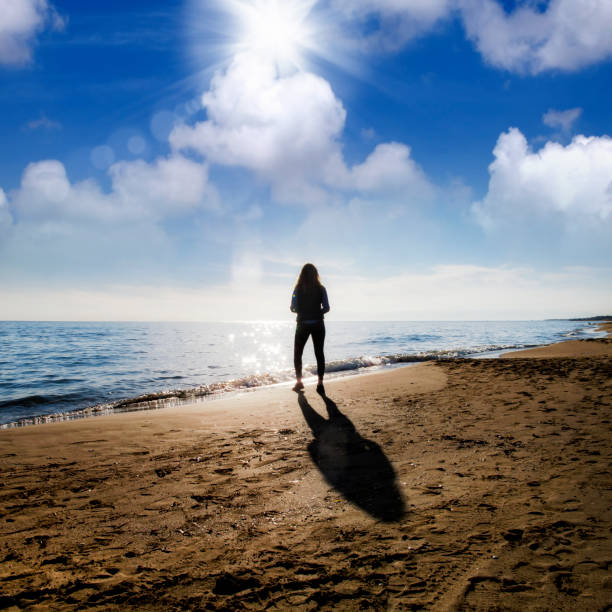 istock Young woman walking on sandy beach over sunny sky 998421852