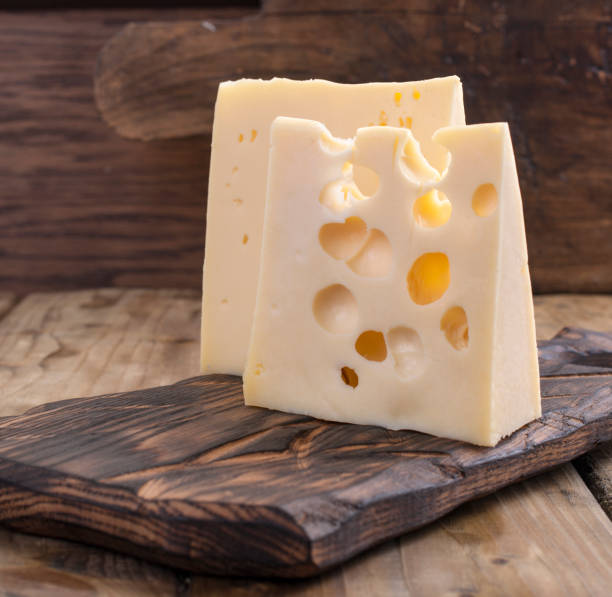 cheese with holes is cut into portions on a wooden board, a useful dairy product. tasty food. country style photo. place for text. copy space - cheese emmental cheese switzerland grated imagens e fotografias de stock