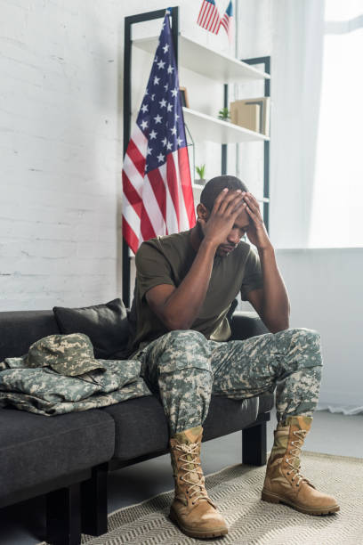 istock Upset army soldier sitting on sofa with camouflage clothes 998429350