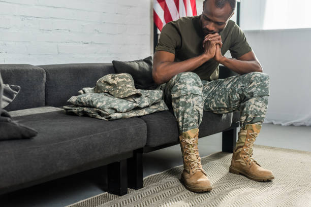 istock Thoughtful soldier sitting on sofa and looking at his camouflage clothes 998429356