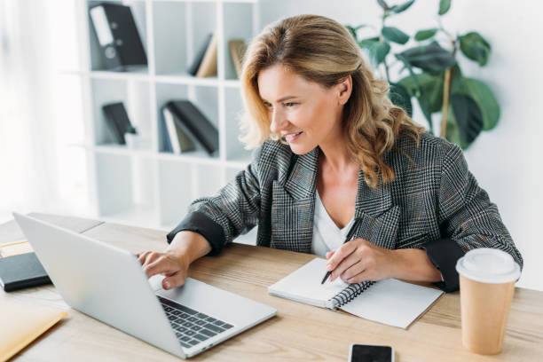 istock attractive businesswoman using laptop and writing something to notebook in office 998433458