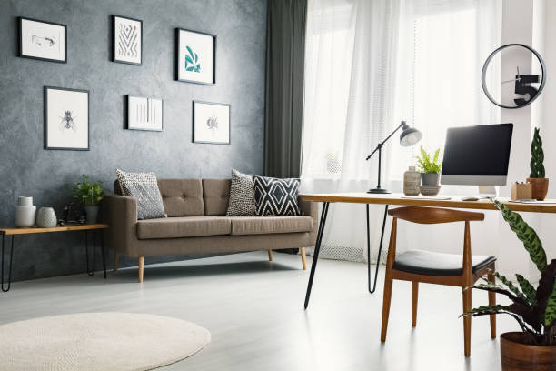 istock Remote work corner desk in living room interior with raw wall with posters, couch with pillows and window with drapes 998440932