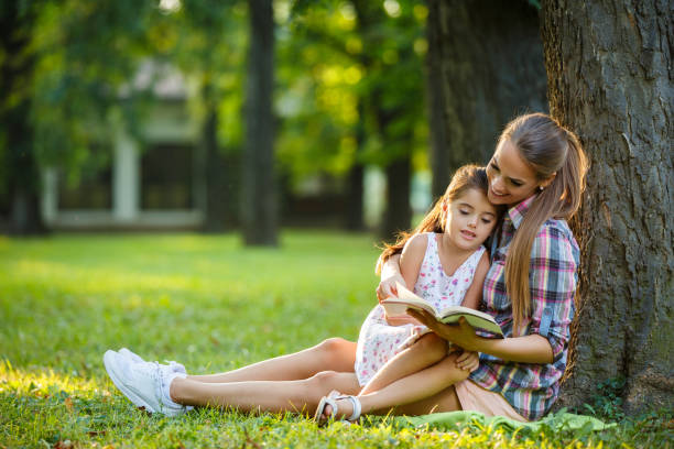 istock Mother and daughter sitting on grass reading a book 998450658