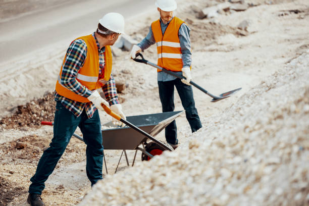 istock Men in uniform with shovels pouring sand into wheelbarrow during dirty work 998457070
