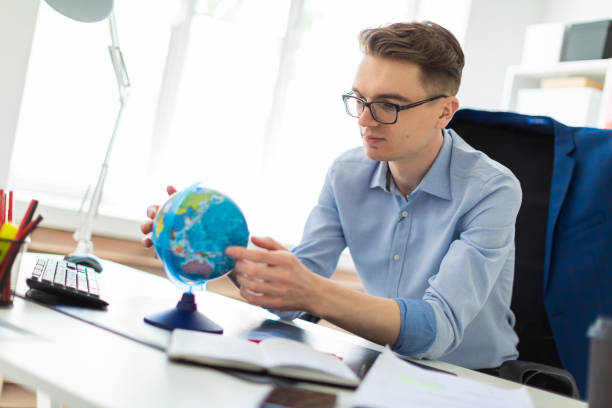 istock A young man sits in the office at a computer desk, looks at the globe and thinks. 998457208