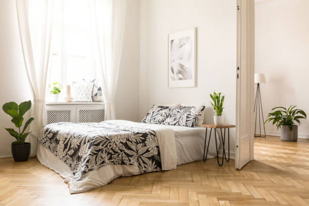 istock Poster above bed with patterned cushions in bright bedroom interior with window and plant. Real photo 998461050