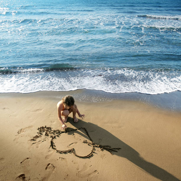 istock Happy little girl drawing heart shape on sandy beach 998476580