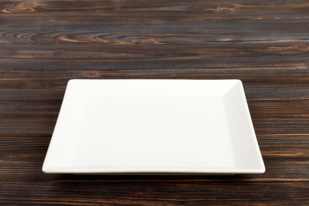 istock Empty square white plate in wood background, food display montage. Perspective view 998478076
