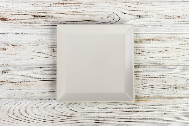istock Square white empty plate on white wooden background. Top view 998478088
