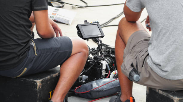 istock Back angle view of high definition digital video camera which recording or shooting tv commercial production on pan tilt shift professional head tripod at outdoor location and film crew team with set. 998488548
