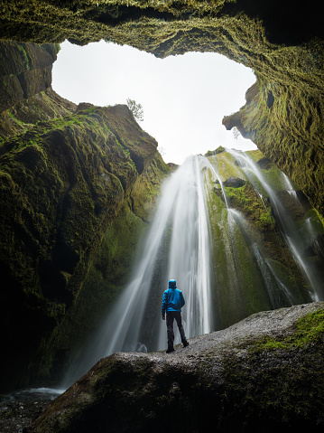 Glyufrafoss waterfall in the gorge of the mountains. Tourist Attraction Iceland. Man tourist in blue jacket standing on a stone and looks at the flow of falling water. Beauty in nature