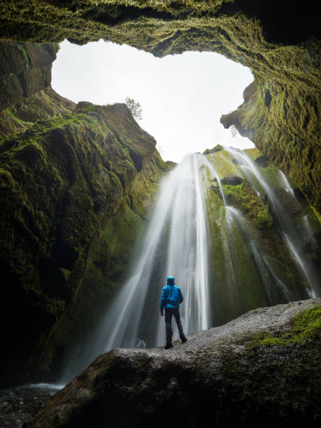 Tourist looks at the big waterfall in Iceland Glyufrafoss waterfall in the gorge of the mountains. Tourist Attraction Iceland. Man tourist in blue jacket standing on a stone and looks at the flow of falling water. Beauty in nature Hidden Meaning stock pictures, royalty-free photos & images