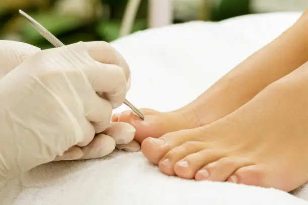 Pedicure master during work. Closeup of female nails and hands in gloves with a special steel tool.