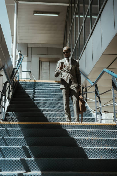 istock Young african american businessman using smartphone while walking on stairs 998505216