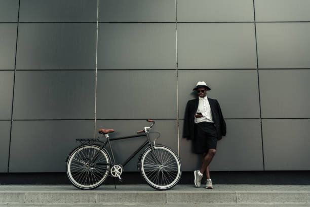 istock Fashionable african american man wearing fedora hat using smartphone while standing by his bicycle 998505406