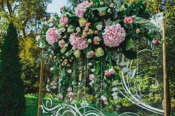 istock Wedding glass arch with white patterns decorations is standing outdoors in the green summer park. Pink hortensia and roses flowers on background. 998509340
