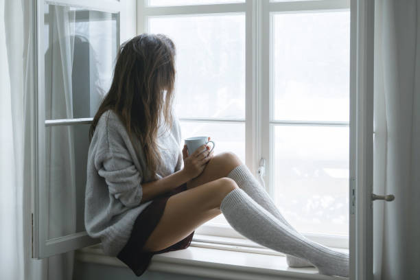 femme est assise sur le rebord de la fenêtre et boire du thé chaud ou café - pull cachemire femme photos et images de collection