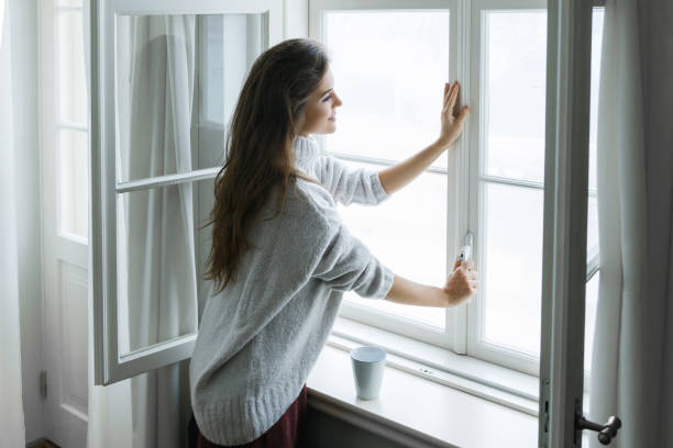 Woman in warm woolen pullover is opening window Woman is opening window to look at beautiful snowy landscape outside window stock pictures, royalty-free photos & images