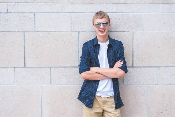 Photo of Happy teen wearing sunglasses and leaning with his back against a brick wall.