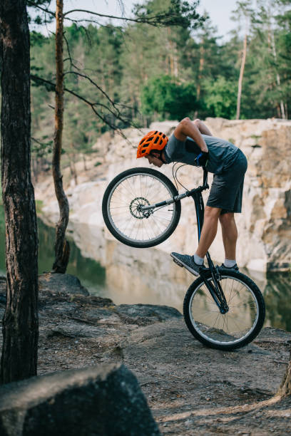 istock young trial biker balancing on back wheel outdoors in front of lake at forest 998548070